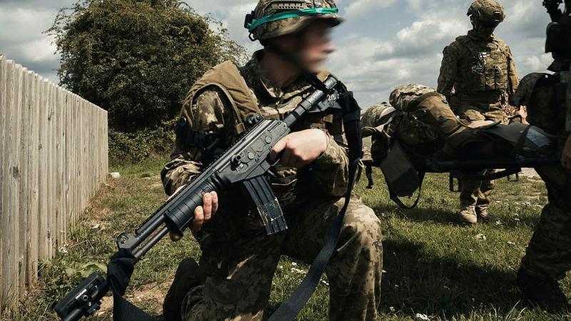 One soldier guards the scene while others carry a simulated casualty on a stretcher.