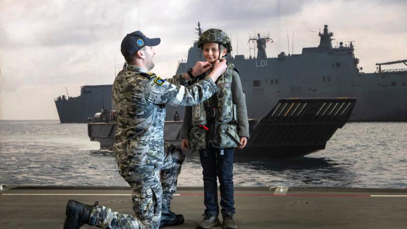 Boatswain’s mate Petty Officer Doug Rowan helps a visiting child put on a protective vest during HMAS Adelaide’s open day in Hobart, Tasmania.