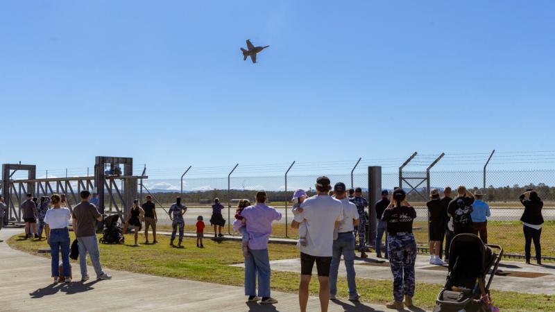 A crowd of people watch an aircraft performing an aerial display.