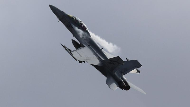 An F/A-18F Super Hornet in the sky, with contrails coming out the sides.