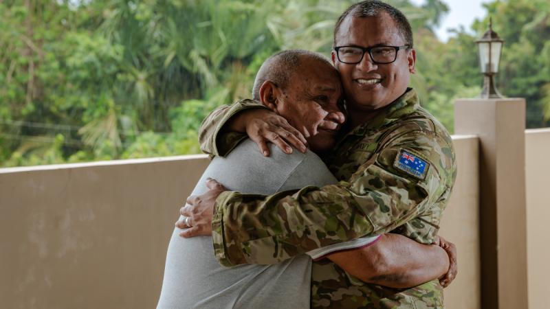 A man in uniform embraces an older man.
