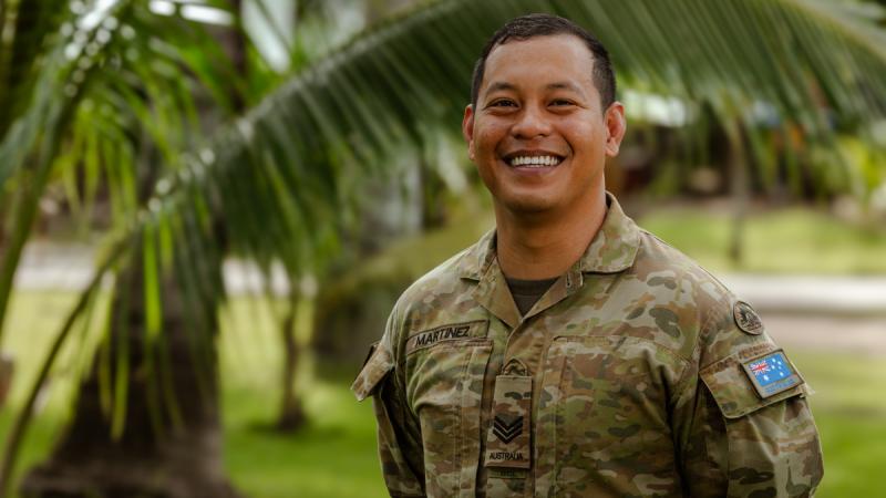 A man in Australian Army uniform poses in a leafy, tropical garden.