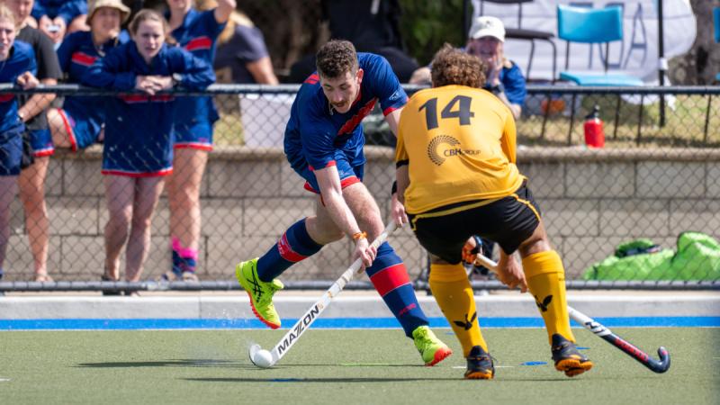 An ADF hockey player in blue plays the ball against a WA players in black and gold.