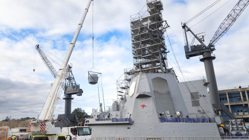 A large object is being lifted off a Navy ship by a crane on the back of a truck.