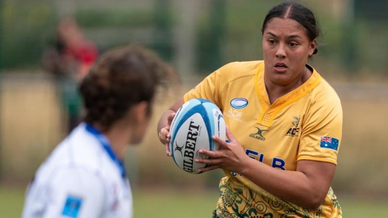 An Australian rugby player in gold jersey runs towards a French defender in white.