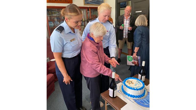 Aircraftwoman Molly Blanch and Leading Aircraftwoman Nicole Webb stand with June as she cuts the first slice of her birthday cake. 