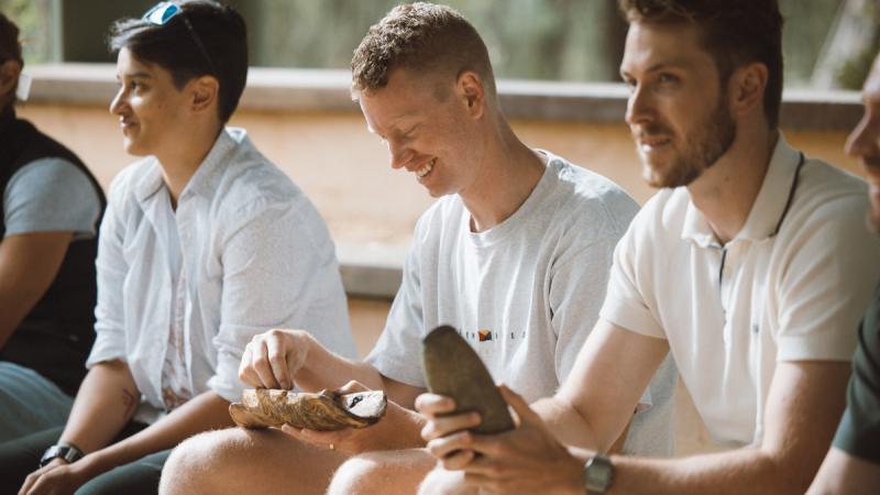 Three men sitting around holding natural wood products.