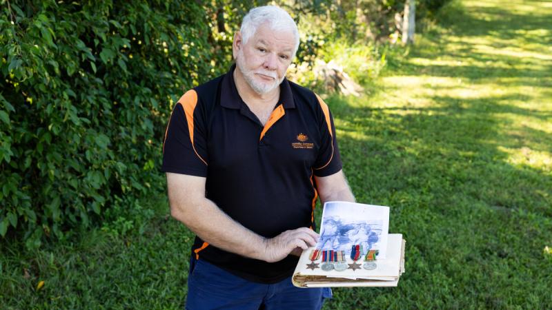 A man standing outside holding medals and a photo album.