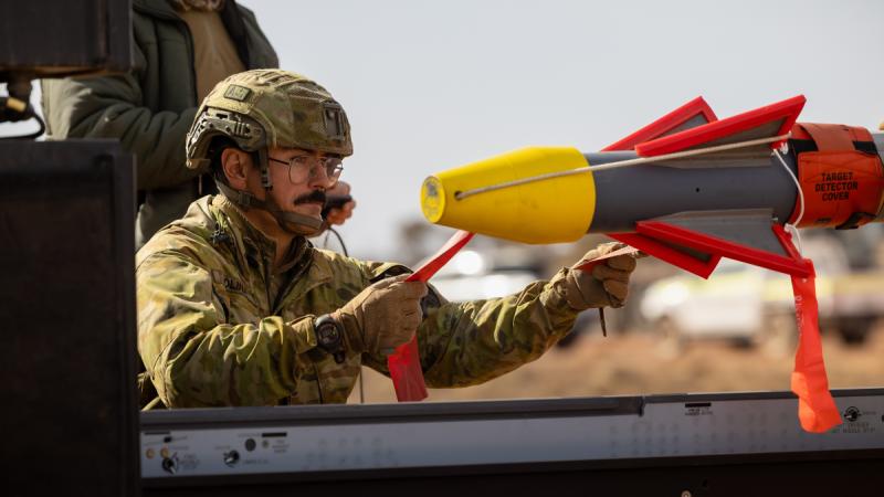A man in full Army fatigues manoeuvring a missile.