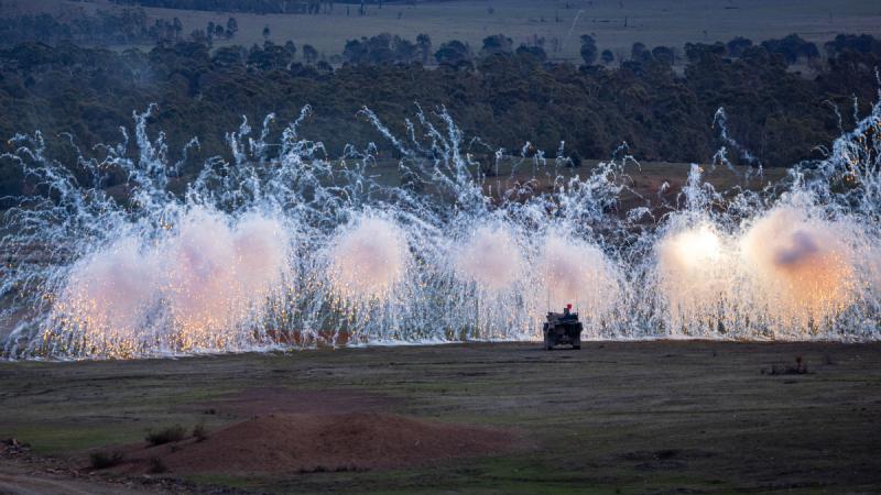 Explosions obscure the movement of an armoured vehicle in the Australian bush.