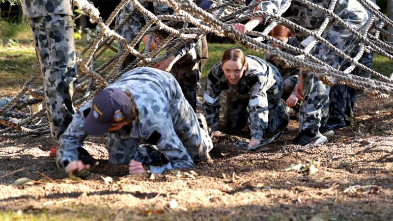 Navy Cadets complete a confidence course, scrambling under a rope net.