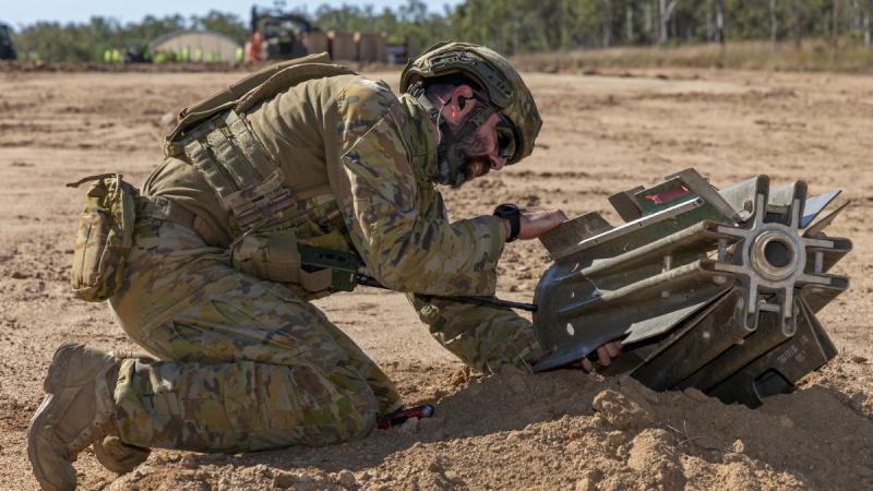 A military man kneeling in the dirt and working on a bomb.
