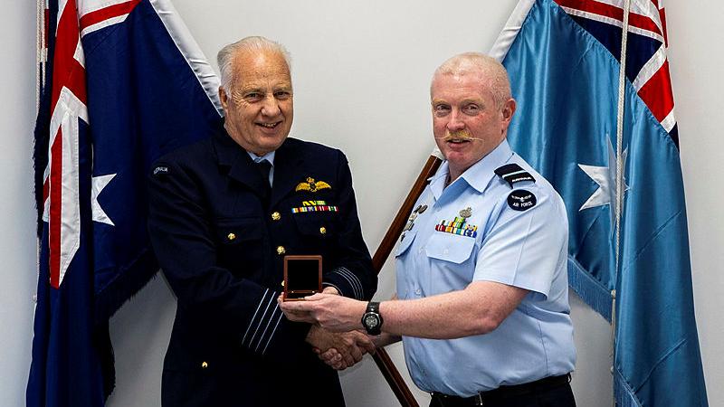 One man in uniform presents another man in uniform with a award.
