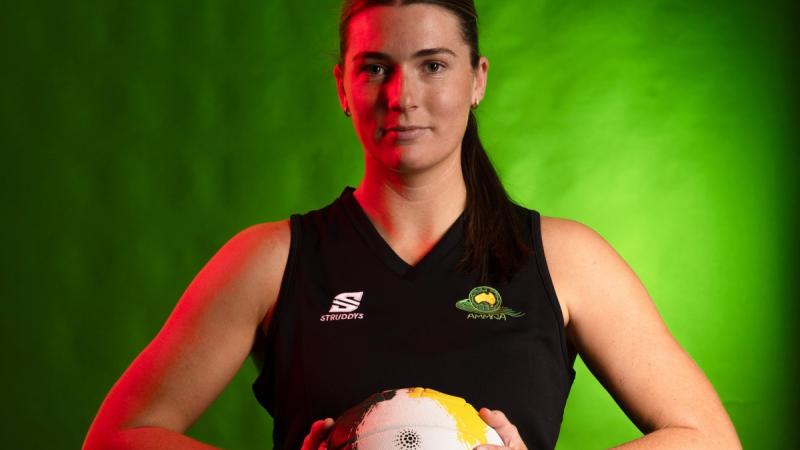 Netballer stands against a green background with ball in both hands.