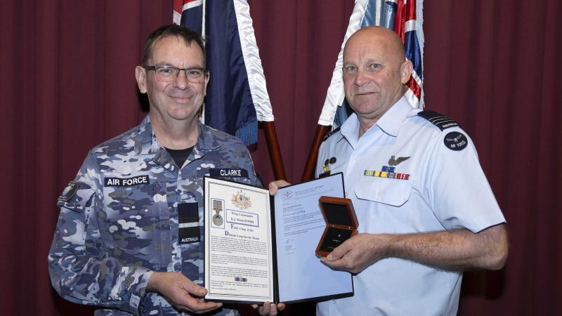 Two men in uniform holding a certificate booklet and a medal.