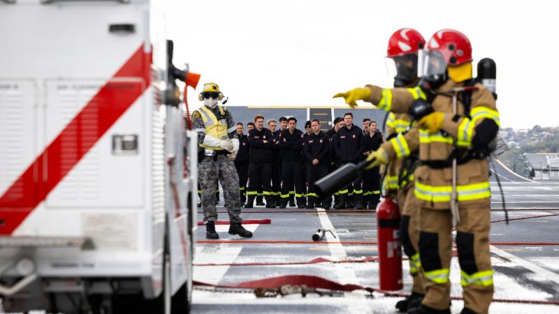 Navy firefighters deploy hoses on the deck of a land helicopter dock ship.