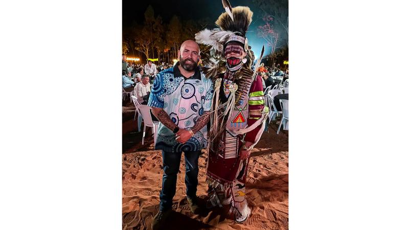 A man stands next to an Indigenous person in cultural attire. 