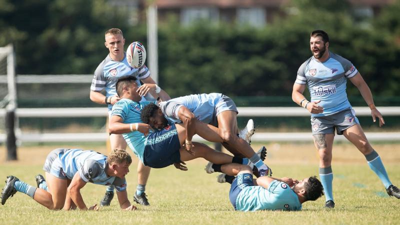 One rugby league player tackles another surrounded by four other players.