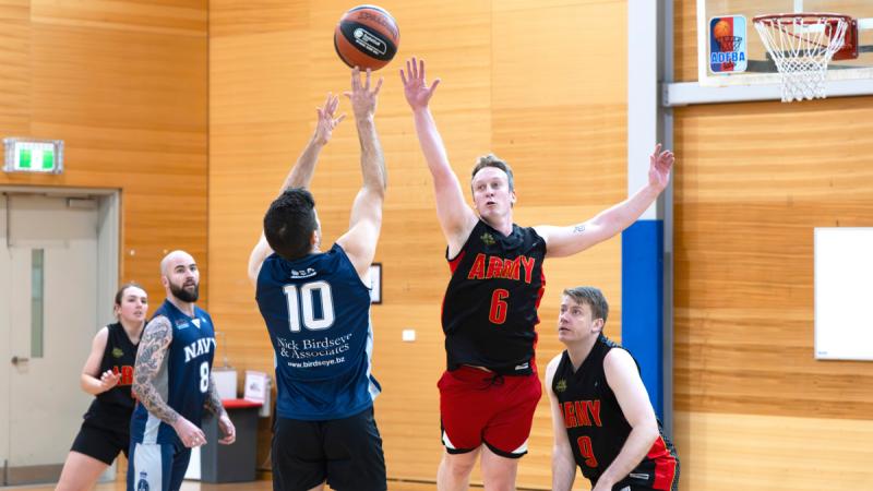 An Army basketball players jumps to defend the ball being thrown by a Navy player.