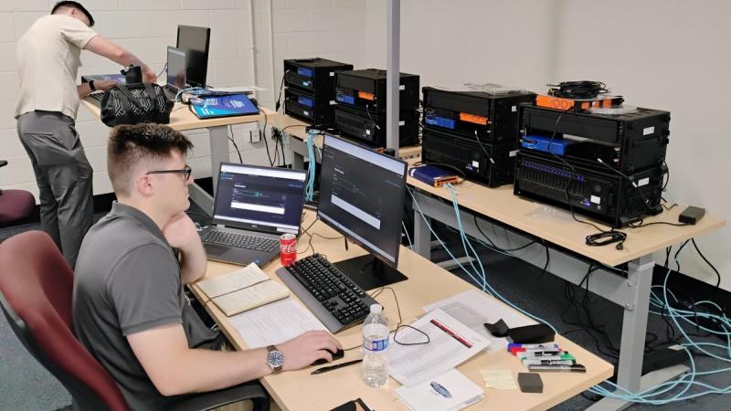 Cyber analysts test defensive systems in a room with banks of computers. 