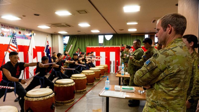 Japanese drummers, left, perform for military personnel in camouflage uniforms in a low-ceiling room.
