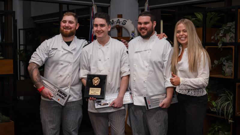 Four Navy chefs in white with guest judge after winning their cooking competition.