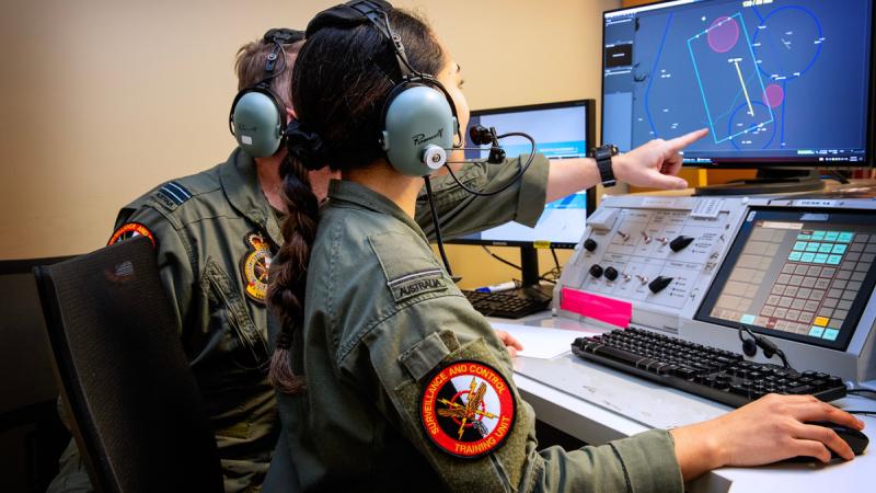 Two Air Force personnel in flying suits track aircraft movements on a computer screen.