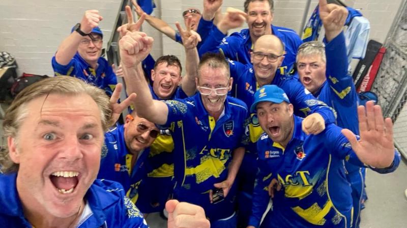 Veterans cricketers dressed in blue celebrate a victory with fist pumps and cheers.