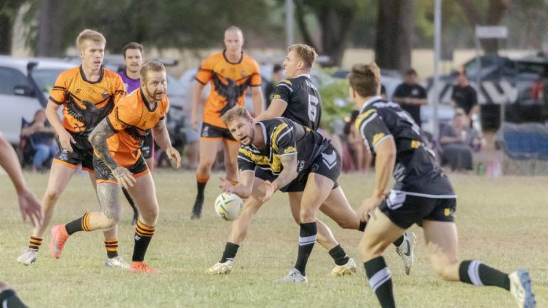 A rugby league player passes the ball down the line during a charity game.