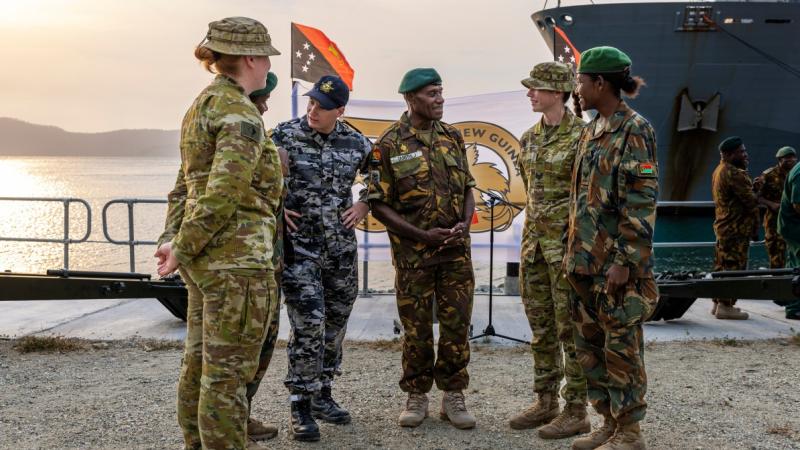 Men and women in ADF and Papua New Guinea Defence Force uniforms chatting in front of a ship.