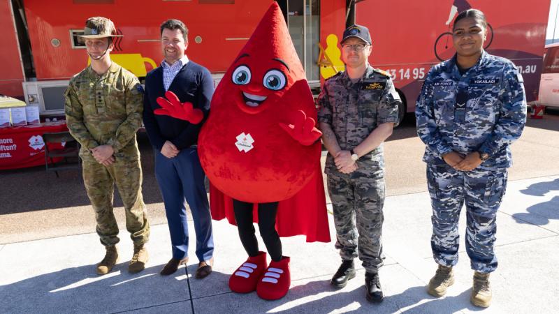 Defence personnel stand alongside a blood-drop mascot to launch a blood donation drive.