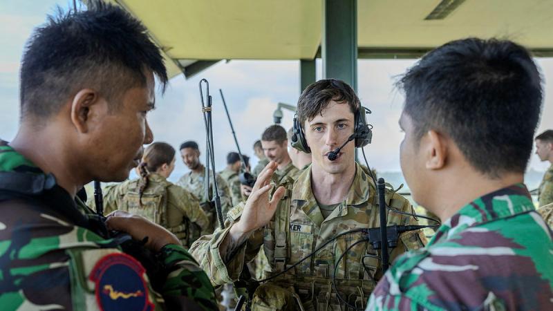 An Australian soldier with a head set on speaks to two Indonesian soldiers.