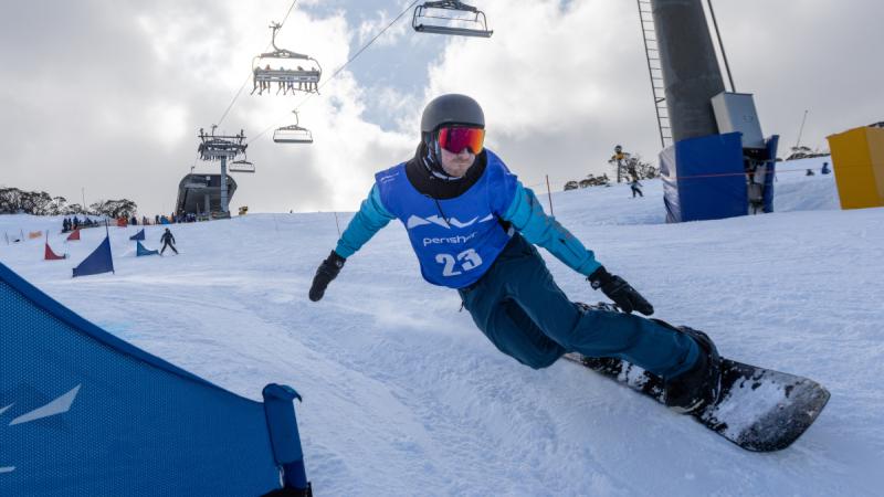 A man in blue outfit snowboards alongside a ski lift carrying skiers .