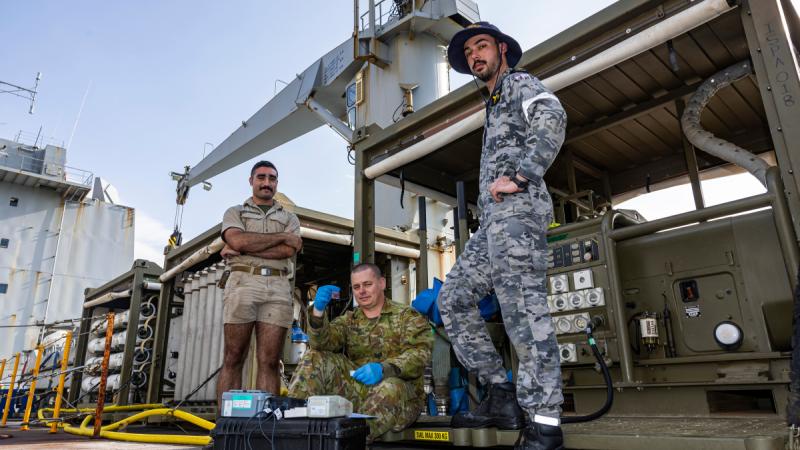 Two soldiers and a Navy technician work on deck to produce clean water.
