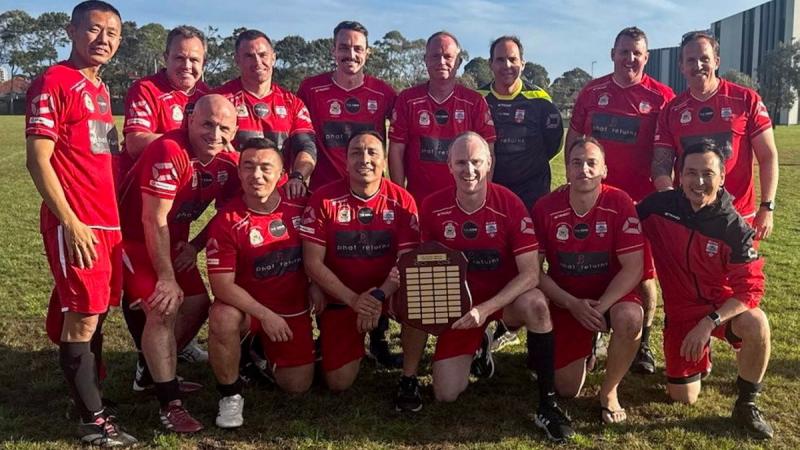 Members of a men’s football team wearing their uniforms and holding an award plaque.