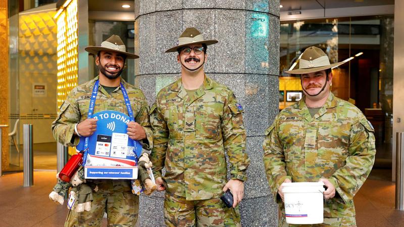 Three soldiers stand in front of a pole and hold collection boxes for Legacy.