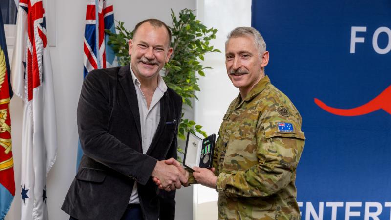 Two men shaking hands as one presents the other with a medal.