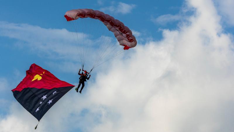 A parachutist descends with a PNG flag.