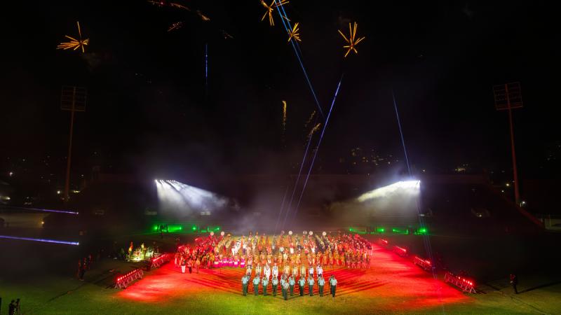 A Military Tattoo taking place in a stadium field with fireworks in the night sky.