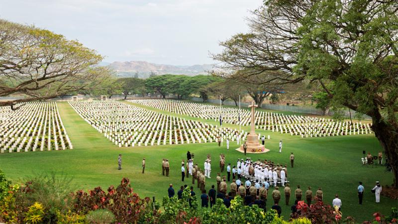 An aerial photograph of the cemetery, with gravestones grouped in three large sections in a green, tree-filled, tropical setting with mountains in the background.