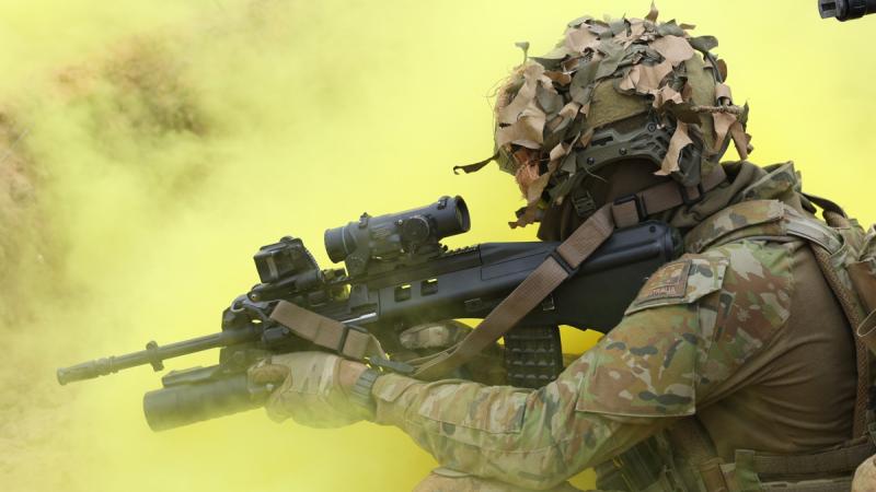 A soldier is surrounded by yellow smoke as he crouches and aims his weapon.