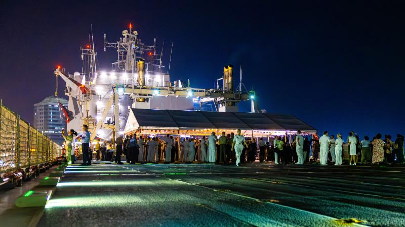 A night-time party held under a marquee on the deck of a ship, illuminated by bright lights.
