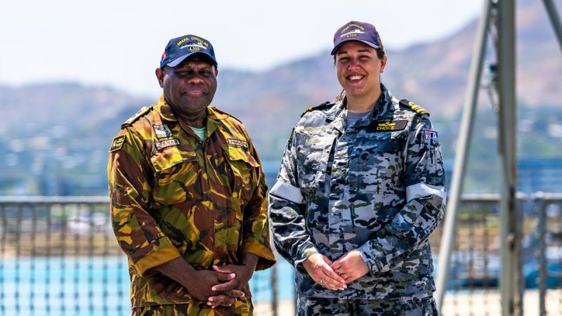 Two smiling people in military fatigues stand side by side on board a ship.