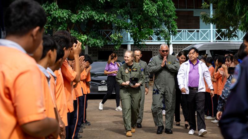 People in uniform walk down a path formed by school children.