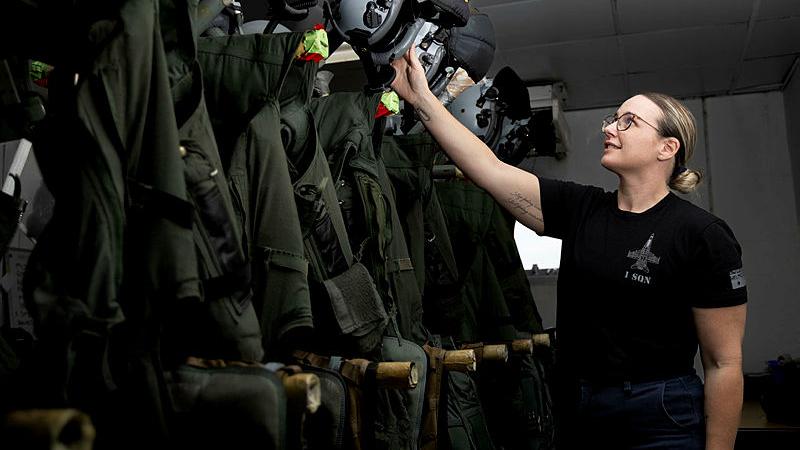 A woman in Air Force clothing checks a line-up of uniforms and helmets.