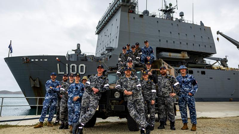 A group of ADF personnel pose around a military ambulance in front of a ship.