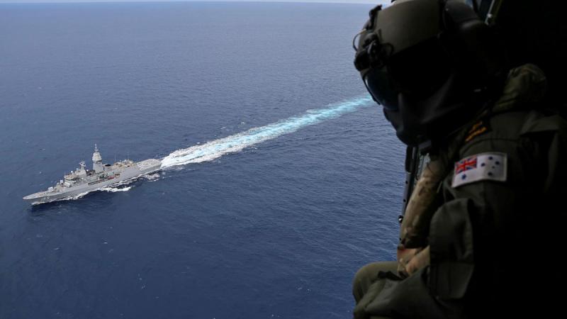 A person in uniform looks out an aircraft at a ship at sea.