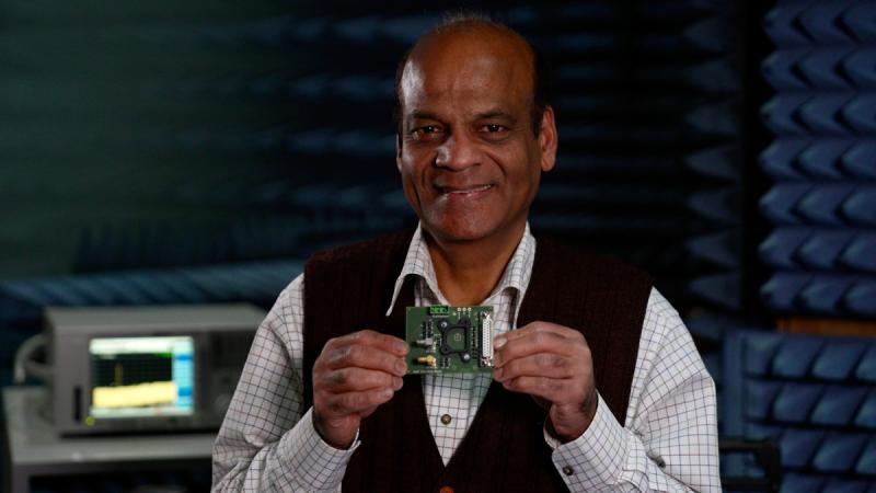 A man in a white shirt and waistcoat holds a computer chip in his hands and smiles for the camera.