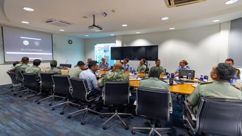 People in uniform sitting around a workshop table looking at the screen at the front of the room.