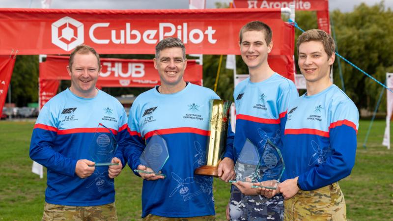 Four soldiers in team uniform hold trophies from the Military International Drone Racing Tournament.